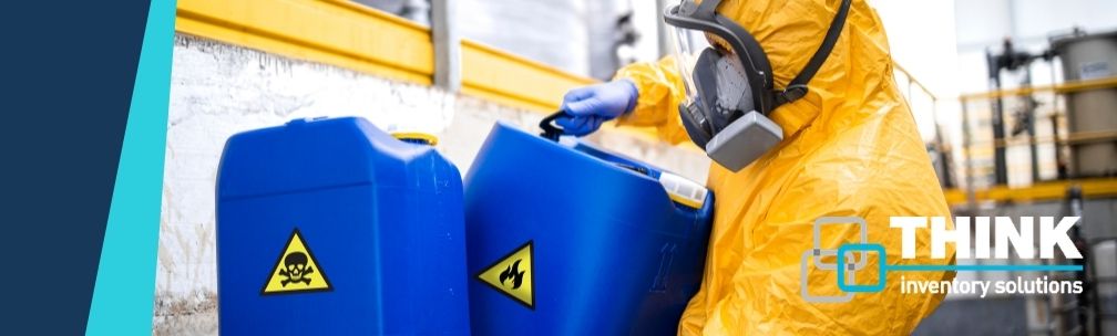 A person in yellow overalls and a face mask moves a blue container with a toxic skull and crossbone warning on the side