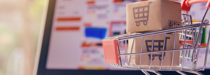 Miniature shopping trolley containing two small cardboard boxes, sat in front of a computer screen