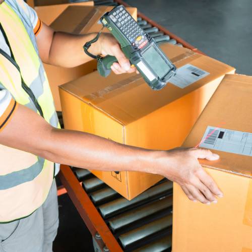 Someone scanning barcoded labels on cardboard boxes on a warehouse conveyor belt