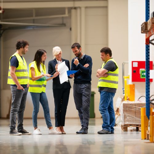 Five workers discussing some paperwork in a warehouse