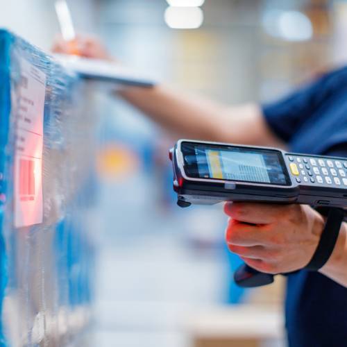 Someone operating a handheld barcode scanner in a warehouse, scanning a barcode on some stock