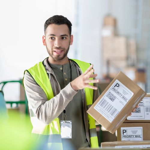 A person holding a cardboard box with a barcode and the words 'priority mail' on the label