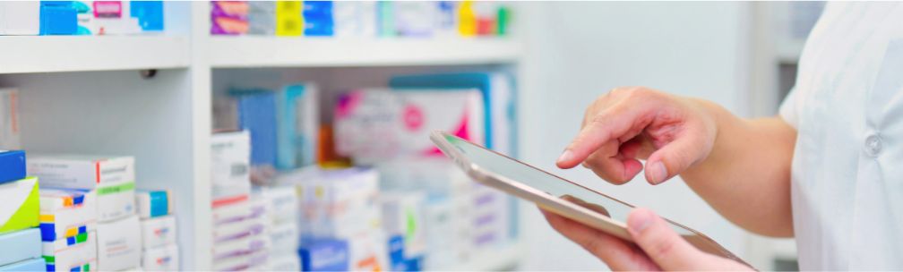 A person stands in front of medicines and tablets on shelving, and checks a computer table