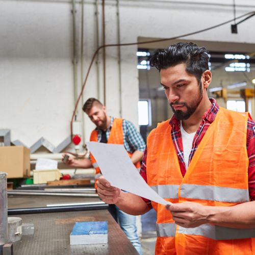 Two warehouse workers in orange high visibility clothing studying paperwork