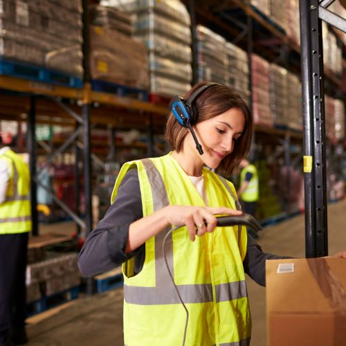 Warehouse worker scanning a barcode on a cardboard box wearing yellow high visibility clothing and a headset
