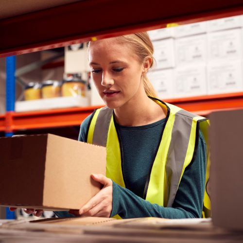A warehouse worker in high visibility clothing taking a cardboard box off industrial shelving