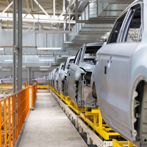A row of silver cars on a factory production line waiting to be built and finished