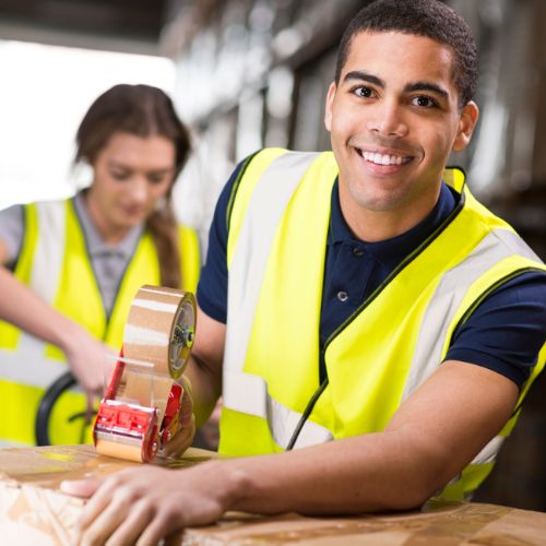 Two warehouse workers in yellow high visibility clothing taping up cardboard boxes