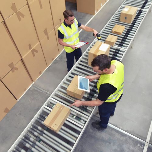 Two warehouse workers in yellow high visibility clothing, one scanning boxes, one looking at the camera holding a clipboard