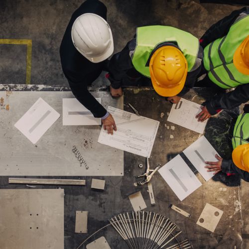 Overhead view of workers in yellow high visibility clothing and hard hats discussing plans on a desk