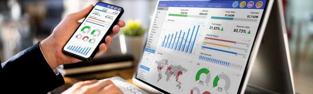 A person holds a tablet and sits in front of a screen showing KPIs and analytics